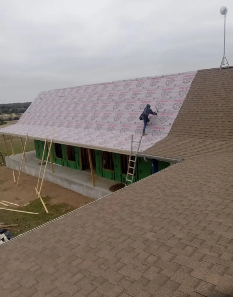 Worker preparing underlayment for a metal roof installation in Walton
